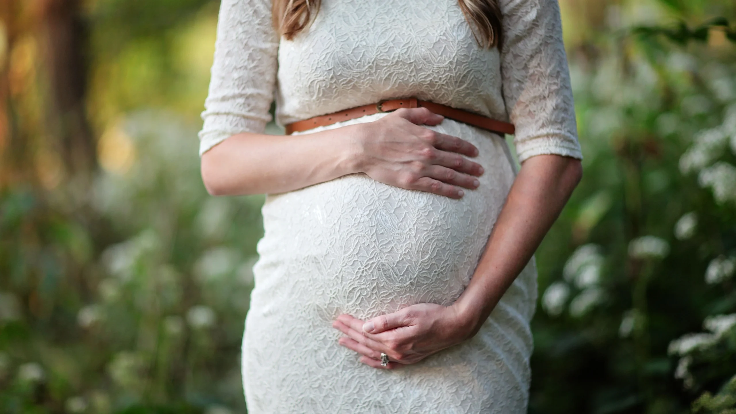Une femme enceinte tient son ventre, lumière naturelle en extérieur