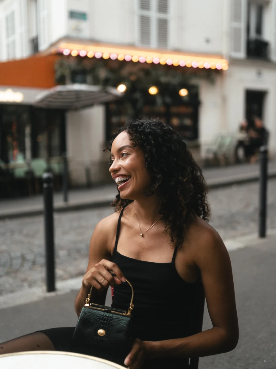 Jeune femme riant à la terrasse d'un café à Montmartre, sac à main à la main